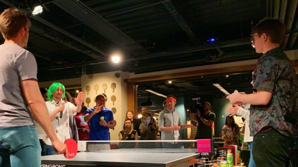 Millenials participating in 826DC's Paddlestar Galactica ping-pong tournament stand around a table at SPIN DC.