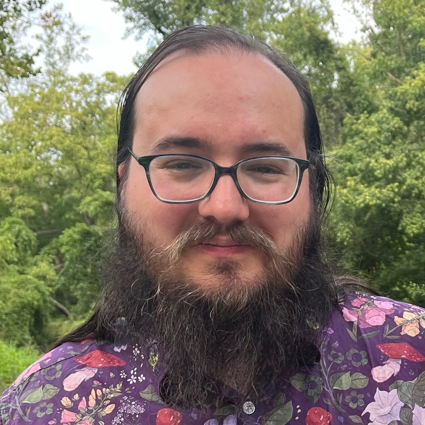 Conor Murphy has a long beard, glasses, and a purple flowered shirt.